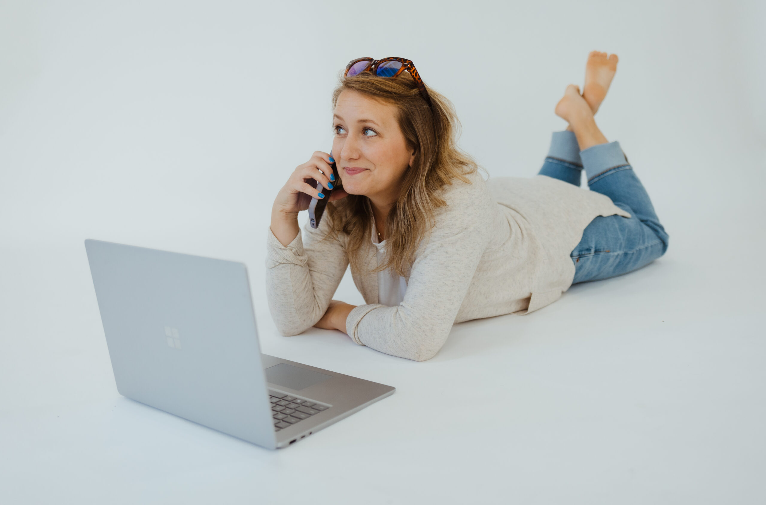 woman laying on ground, phone in hand, with a laptop sitting in front of her, opened